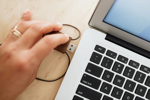 A hand plugging a wooden USB drive into the side of a laptop.