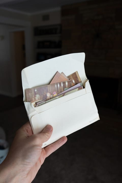 A hand holding an old drugstore photo envelope with prints still inside it.