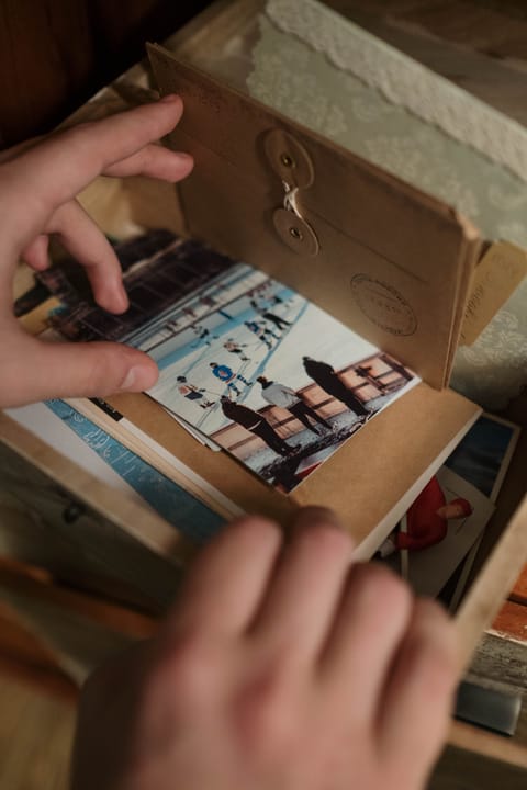 Hands lifting old photographs out of a worn cardboard box of family snapshots.