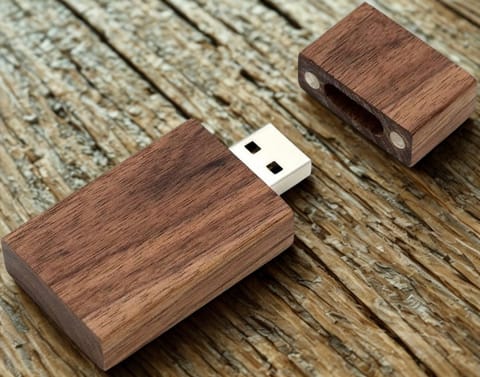 A walnut USB flash drive with its wooden cap lying beside it on weathered wood.